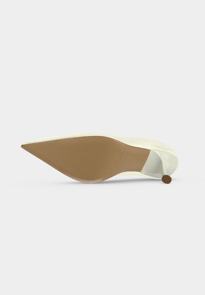 Λευκό γυναικείο παπούτσι με μυτερή μύτη και ψηλό τακούνι, εμφανιζόμενο από τη σόλα με μπεζ χρωματιστό πάτο και μικρό τακούνι στιλέτο.