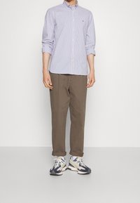 Chemisebutton-up rayée bleu clair, pantalon marron à coupe décontractée et baskets bleu marine et blanches. La chemise a des manches retroussées ; design simple.