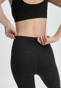 Zwarte sportlegging met een slim fit ontwerp, hoge tailleband en zichtbare stiksels, gecombineerd met een zwart crop top.