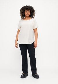 Light beige short-sleeve shirt with a round neckline, worn with black pants and chunky black shoes, against a plain white background.