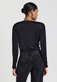 Schwarzes langärmliges Oberteil mit glattem, figurbetontem Design, kombiniert mit hoch taillierten, ausgewaschenen schwarzen Jeans mit Gesäßtaschen und subtiler Textur.