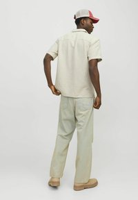 Camisa de cuadros de manga corta en beige y verde, combinada con pantalones de mezclilla claros y calzado beige, vista desde la parte trasera.