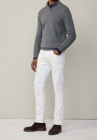 Un sweat à zip gris, un pantalon blanc et des chaussures marron foncé. Le sweat a des poignets côtelés et le pantalon est ajusté avec des poches discrètes.