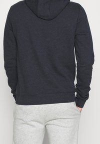 Haut à capuche bleu marine avec une finition texturée, doté d'une capuche à cordon et de poignets côtelés, associé à un pantalon de jogging gris.