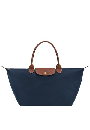 Marineblaue Tote-Tasche mit braunen Ledergriffen und Klappe, goldfarbenem Knopfverschluss und weitem Reißverschluss oben.
