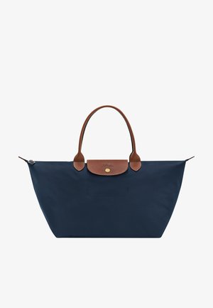 Marineblaue Tote-Tasche mit braunen Ledergriffen und Klappe, goldfarbenem Knopfverschluss und weitem Reißverschluss oben.