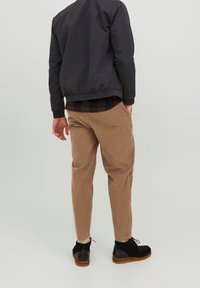 Czarna kurtka bomberka, brązowe sztruksowe spodnie oraz czarne buty z brązową podeszwą. Widoczne przeszycia i kieszenie na spodniach.