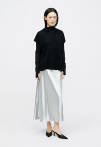 Μαύρο πλεχτό hoodie, γκρι μάξι φούστα σε στυλ μεταξιού με γυαλιστερή υφή, και μαύρες σχεδιαστές γόβες. Ορατά μακριά μανίκια κάτω από το τοπ.