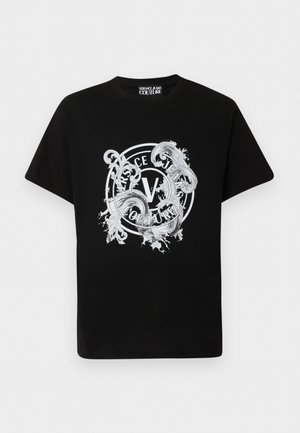 Svart T-skjorte med korte ermer med hvit, sirkulær Versace Jeans Couture-logo og utsmykket barokk-inspirert snirkeldesign på forsiden.