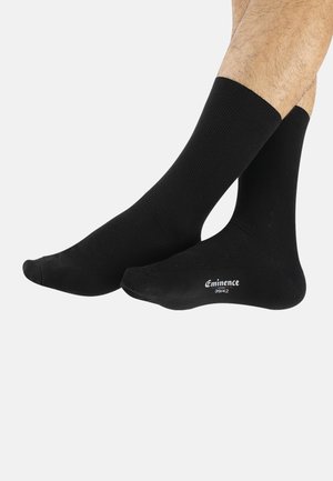 Chaussettes en coton noir avec une texture côtelée, dotées d'un bord confortable. Le nom de la marque "Eminence" est imprimé en blanc sur la zone de la cheville.