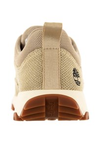 Beige sneaker met een bovenwerk van gaas en stoffen accenten, met een trekbandje aan de hiel en een bruine rubberen buitenzool met een gestructureerd profiel.