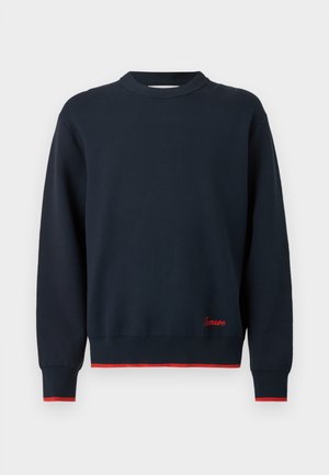 Marineblå langærmet sweater med rund hals, rød kant ved ærmer og kant, og lille rød broderi over kanten på forsiden til højre.