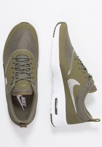 Ett par olivgröna Nike Air Max-sneakers med vita sulor, nät- och syntetmaterial, samt synlig luftdämpning på en vit bakgrund.