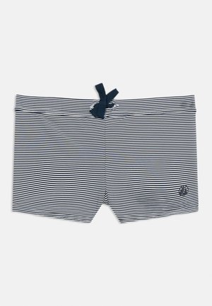 Tengerészkék és fehér csíkos fürdősort, elöl húzózsinórral és kicsi vitorláshajó logóval az alsó jobb lábszáron.