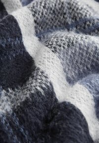 Couverture en tricot bleu marine et blanc avec un motif à carreaux, mettant en avant des fils doux et texturés ainsi qu'une apparence superposée.