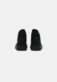 Černé kotníkové boty s měkkým textilním svrškem, pevnou gumovou podrážkou a elastickými bočními panely pro snadné obouvání. Zpětný pohled ukazuje bezešvý design.