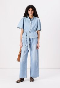 Light blue denim jacket with wide sleeves, button front, and belt. Paired with wide-leg jeans and animal print flats. Brown shoulder bag.