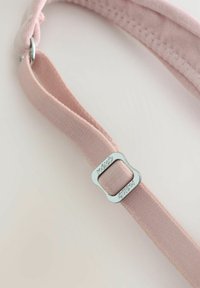 Rožinė audinio juosta su lygia tekstūra, turinti blizgantį sidabrinį metalinį sagtį su raižytais akcentais. Artimas vaizdas, išryškinantis detales.