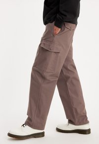 Kargo kalhoty v tlumené mauve, nabízející boční kapsy a uvolněný střih. Vyrobené z odolné látky se subtilními švy. Nalezené s bílou obuví.