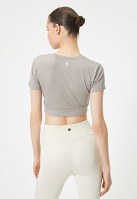 Top grigio chiaro a maniche corte, di tessuto morbido, con un piccolo logo sul retro. Abbinato a leggings giallo pallido a vita alta.