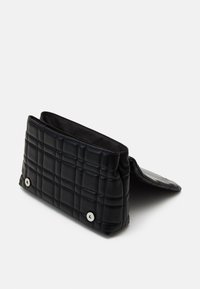 Pochette rectangulaire matelassée noire avec rabat et deux boutons-pression argentés, présentée ouverte sur fond blanc.