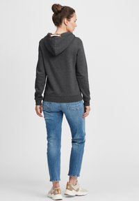 Mørk grå hettegenser med snøring og tremekanisme, sammen med lyseblå jeans og beige sneakers. Stoffet ser mykt og behagelig ut.