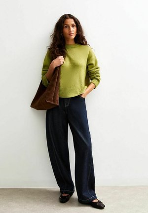 Maglione verde a maglia, jeans larghi blu scuro e borsa in suede marrone. La trama del maglione è morbida; la borsa presenta una finitura liscia.