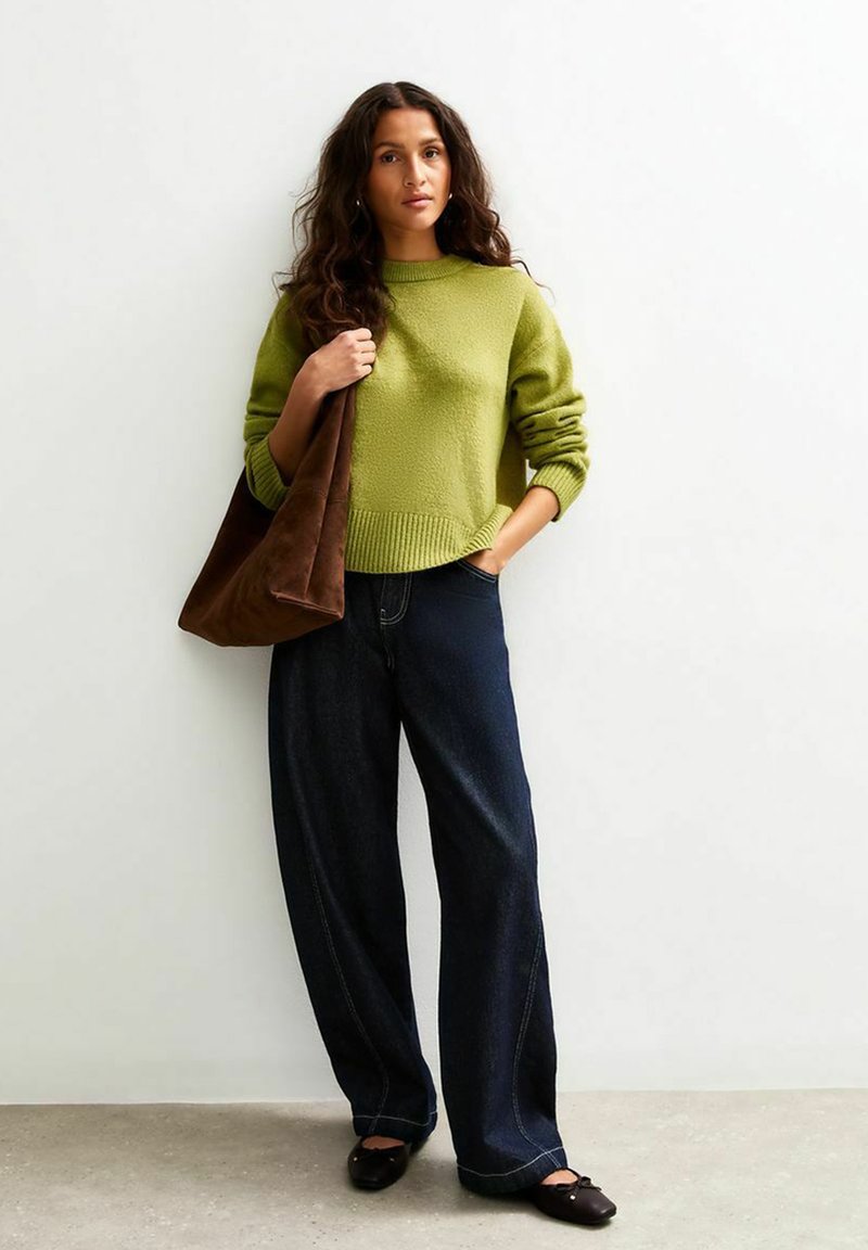 Un pull en tricot vert, un jean large bleu foncé et un sac en daim marron. La texture du pull est douce ; le sac a une finition lisse.