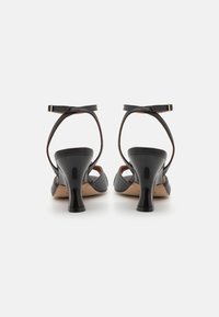 Black leather high-heeled sandals with a curved block heel, adjustable ankle straps, and a smooth texture. Sole is nude color.