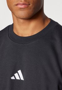 Sweatshirt preto com um decote redondo canelado, apresentando um distinto logótipo triangular branco na frente. Textura de algodão suave.