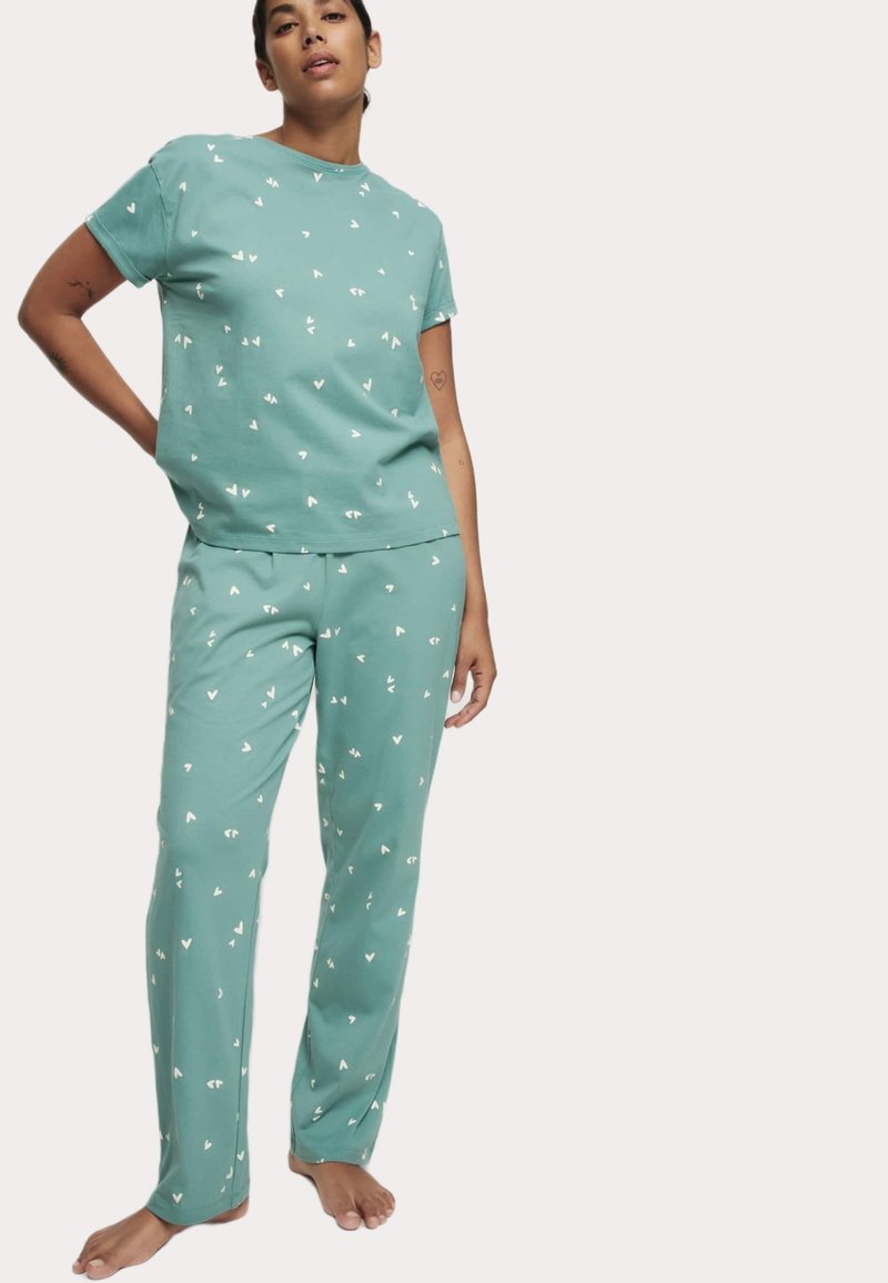Conjunto de pijama en verde claro hecho de una tela suave. Camiseta de manga corta y pantalones largos con pequeños patrones de corazones blancos. Ajuste relajado con un diseño sencillo.
