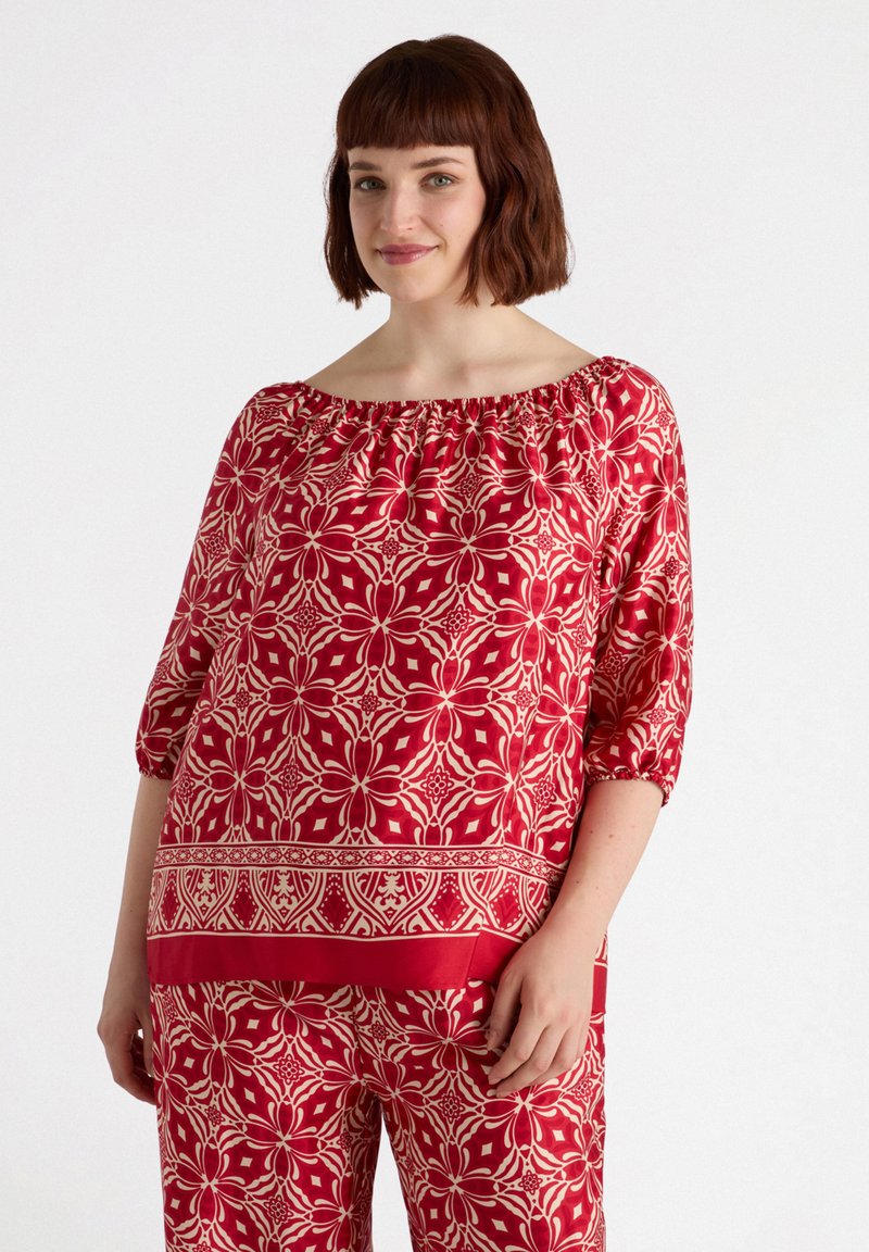 Top rosso scollato sulle spalle con un motivo floreale in crema, maniche a tre quarti e scollatura arricciata. Tessuto dalla texture morbida.