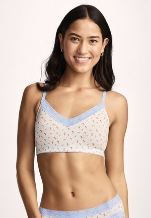 Smiling woman wearing a light-colored bralette and matching underwear with pastel abstract shapes and blue lace trim.