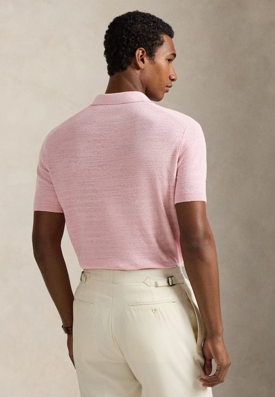 Πόλο μπλουζάκι με κοντά μανίκια σε ανοιχτό ροζ, πλεκτή υφή με γιακά, φορεμένο με παντελόνια σε εκρού χρώμα, με ρυθμιζόμενα πλαϊνά λουράκια.