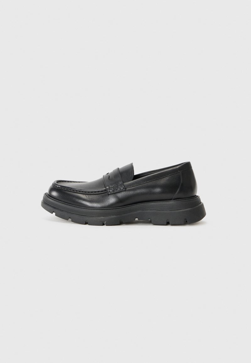 Scarpa nera in pelle scamosciata, con design mocassino, punta arrotondata, suola in gomma spessa e un sottile dettaglio di cucitura nella parte superiore.