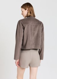 Veste marron courte en matériau doux, au design simple, à coupe droite et à manches longues. Associée à un short beige clair.