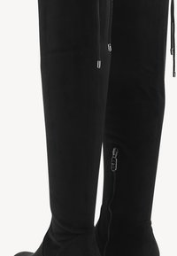 Bottes noires montantes au-dessus du genou en matière suède douce, avec une fermeture éclair latérale, une texture lisse et une coupe ajustée.