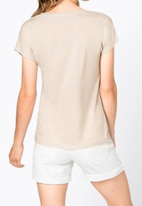 Beżowa bluzka z krótkim rękawem o okrągłym dekolcie, z miękkiego materiału i luźnym kroju, zestawiona z białymi szortami z podwiniętymi nogawkami i tylnymi kieszeniami.