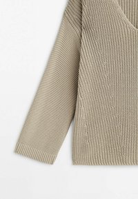 Beige knitted sweater with a V-neckline, textured pattern, and long sleeves. Features ribbed cuffs and hem, showing a relaxed fit.