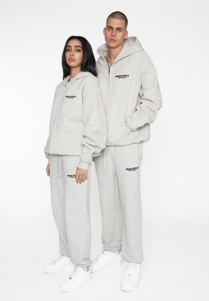 Light gray matching hoodie and sweatpants set, featuring a logo on the chest and pants. The fabric is soft with a relaxed fit. White sneakers complete the look.