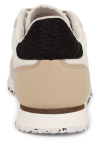 Zadní pohled na béžovou a bílou tenisku s černým texturovaným patním dílem a tečkovanou bílou podrážkou.