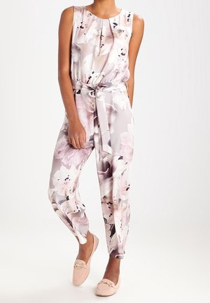 Mono de estampado floral en rosa pálido y crema, con escote fruncido, cintura con cinturón y pantalones de corte relajado. Combinado con bailarinas rosa claro.