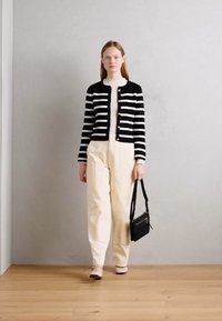 Cardigan à rayures noires et blanches avec des boutons en perles, top crème et pantalon beige clair. Sac à main noir, ballerines neutres, sur un fond neutre.