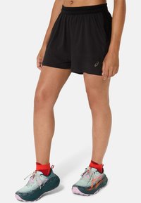 Black athletic shorts with a textured pattern and an elastic waistband. Paired with teal and pink running shoes and red sports socks.