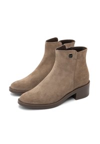 Bottines en suédine marron, avec un bout rond, un léger talon et un accent de logo sur le côté. Texture douce et design minimaliste.