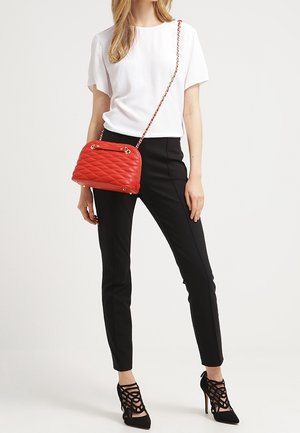 Sac à main matelassé rouge avec quincaillerie dorée et bandoulière en chaîne, posé sur un fond neutre. Présente une forme arrondie et une surface texturée.