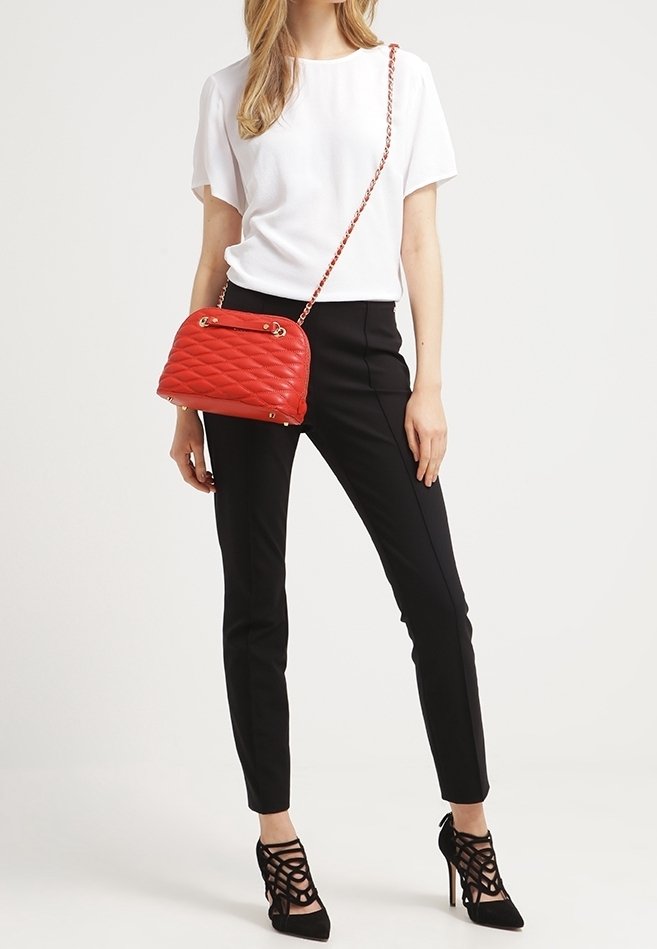 Červená prošívaná kabelka se zlatými detaily a řetízkem, umístěná na neutrálním pozadí. Má zaoblený tvar a strukturovaný povrch.