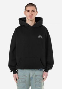 Fleece anyagból készült fekete kapucnis pulóver, elülső zsebbel és kis fehér logóval a mellrészen. Laza szabású, bordás mandzsettákkal.