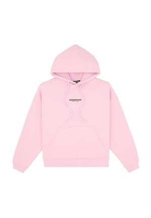 Femme portant des lunettes de soleil noires, un sweat à capuche rose oversize, une mini-jupe noire et des bottes noires souples, debout devant un fond gris uni.