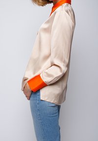 Silk blouse with a light beige body and vibrant orange collar and cuffs. Relaxed fit, long sleeves, and soft, smooth texture.